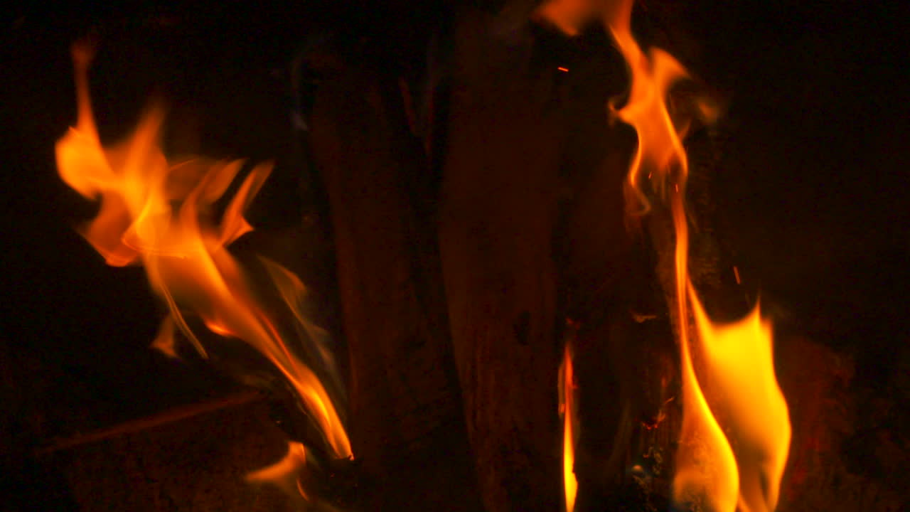 Primo piano al rallentatore di fiamme che bruciano attorno a un tronco in un caminetto.