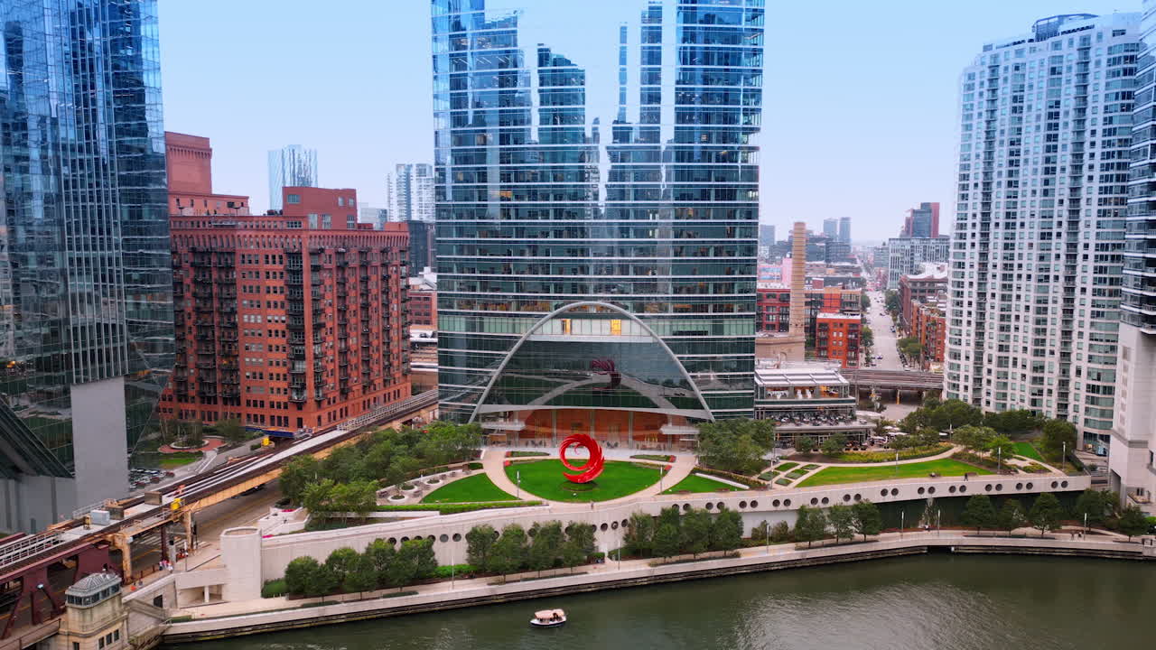 Beautiful park with a red installation at the waterfront of the Chicago River. Modern high-rise buildings around. Chicago, Illinois, USA