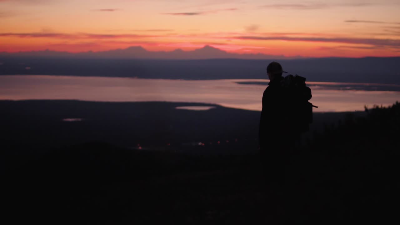 Silhouetted Hiker Walks Down Alaskan Mountain Slope with Sunset in Backround