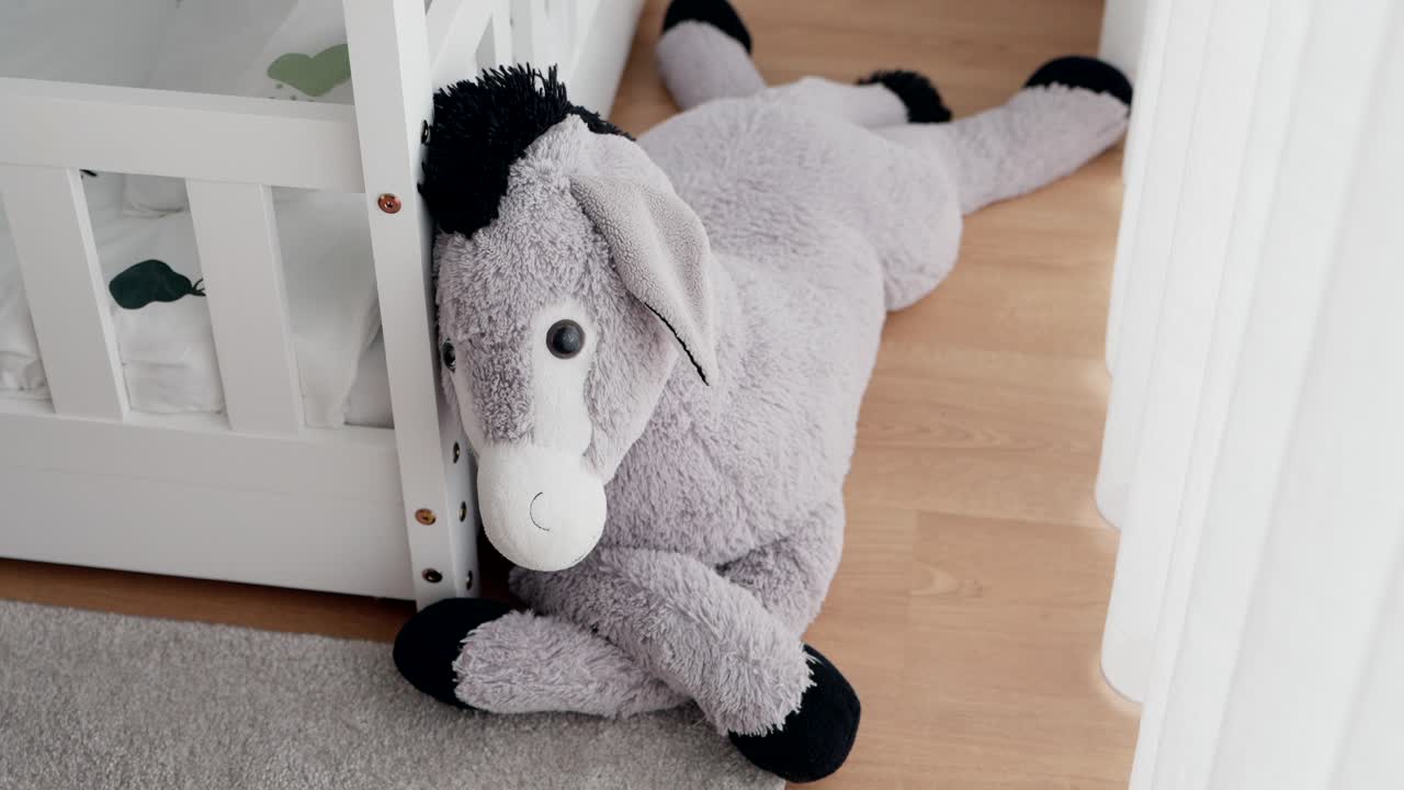 Soft donkey plush toy rests on wooden floor next to crib in cozy room