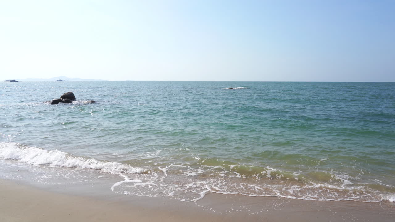 바다와 멀리 떨어진 해안선과 섬에 바위가 있는 맑은 푸른 하늘 날 낮은 파도가 있는 열대 해변에서 바다 전망의 넓은 샷