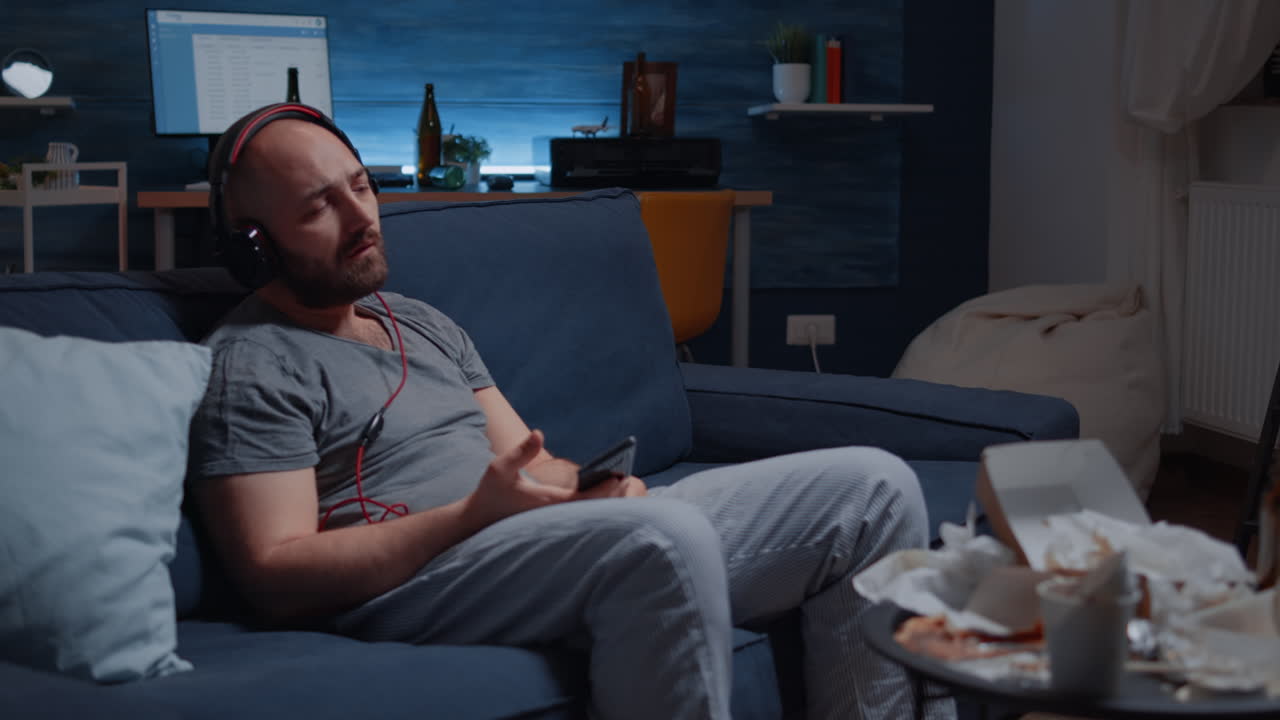 Deprimert mann som hører på musikk med hodetelefoner, sitter alene