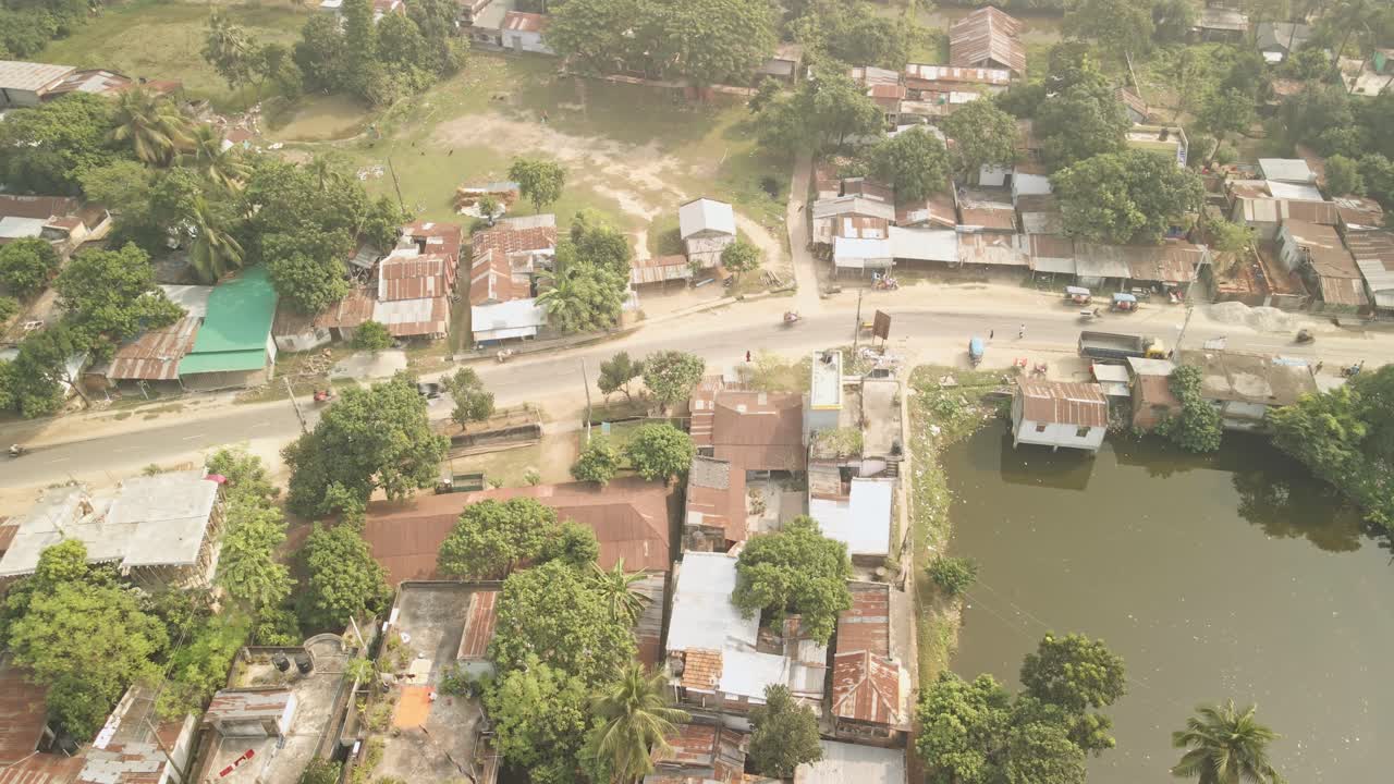 Aerial still drone shot over a Bangladeshi road with rickshaws and local vehicles moving through a lush rural setting.