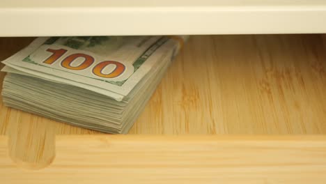 stack of 100 dollar bills in a wooden drawer