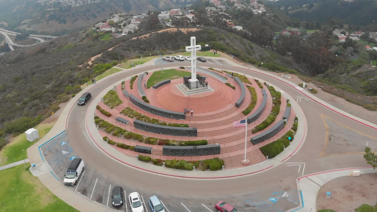 hermosa fotografía aérea rodeando el monte soledad con la cruz, los coches, los árboles, la hierba, las colinas, las casas y la costa a la vista en san diego, california