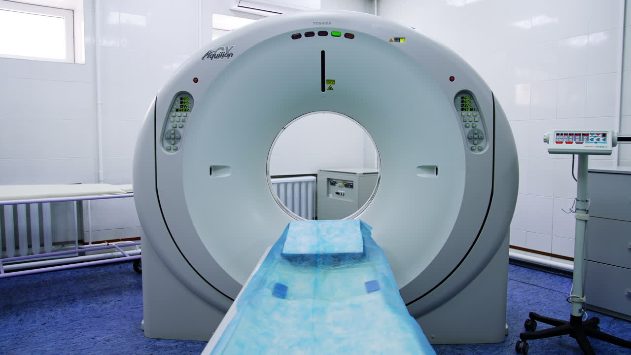 Innovative equipment for magnetic resonance check up in the modern hospital. Toshiba machine with bed laid with blue sheet.