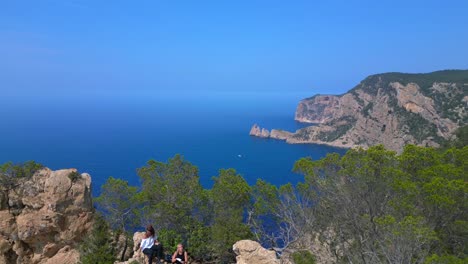 group of tourists hiking on a rocky cliff in ibiza, spain, enjoying the breathtaking view of the mediterranean sea. smooth aerial view flight overflight flyover drone