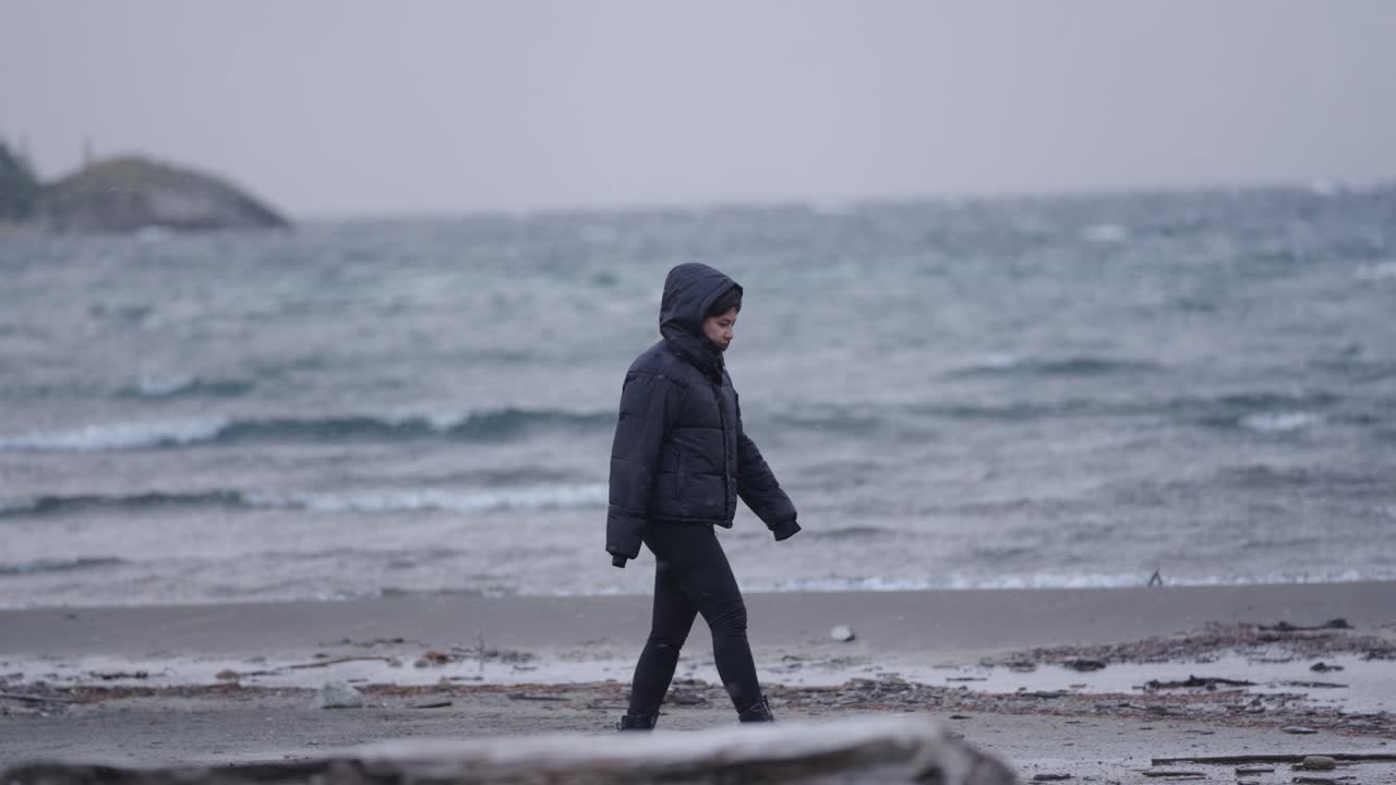 Woman strolling by icy waters of Patagonian Lake under gray skies and winter stillness, Argentina
