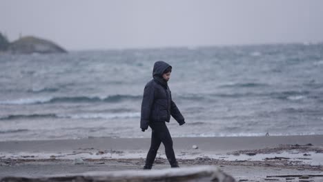 woman strolling by icy waters of patagonian lake under gray skies and winter stillness, argentina