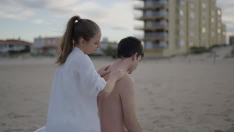 woman giving back massage to man on the beach