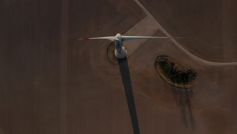 Top-down-shot-of-wind-turbine-in-middle-of-field.-Spinning-rotor-against-brown-soil-in-agricultural-field.-Green-energy,-ecology-and-carbon-footprint-reduction-concept