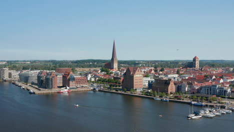 Forwards-fly-above-water-surface.-Aerial-view-of-historic-part-of-town-with-tall-spire-of-Saint-Peters-church