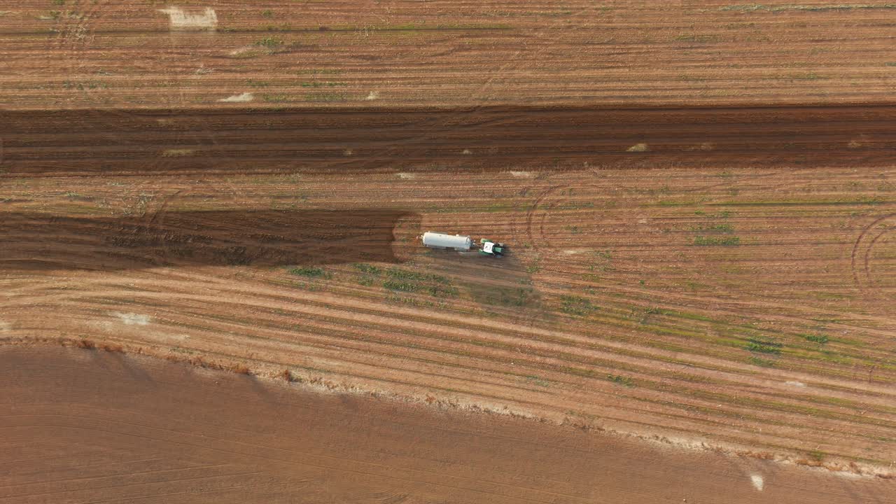 Aerial pan shows tractor driving on vast farmland while fertilizing with natural manure, top down birdseye view