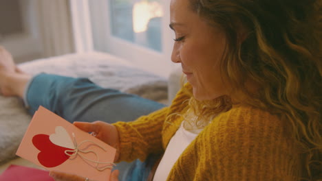 woman in cosy warm jumper lying on sofa at home lying on sofa reading romantic valentines day card