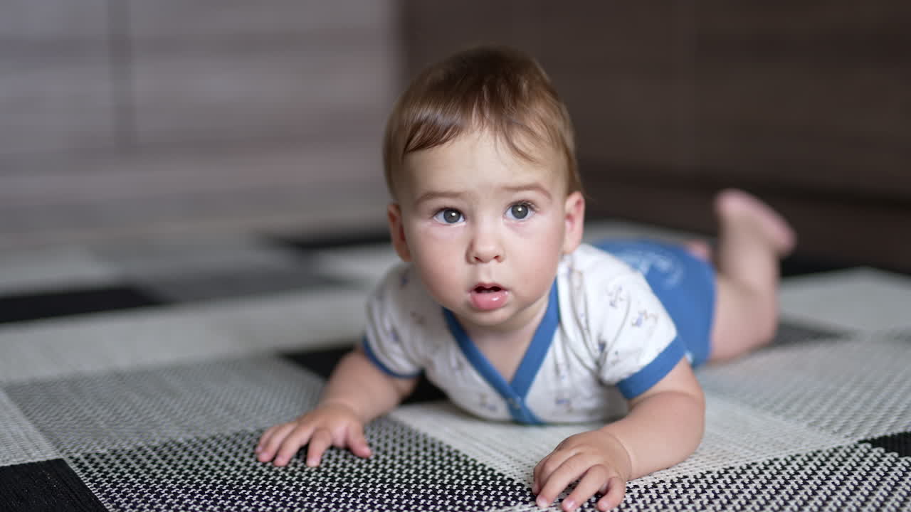 Calm Caucasian little toddler boy lies on his belly on the floor. Lovely kid looking surprised almost not moving. Close up.