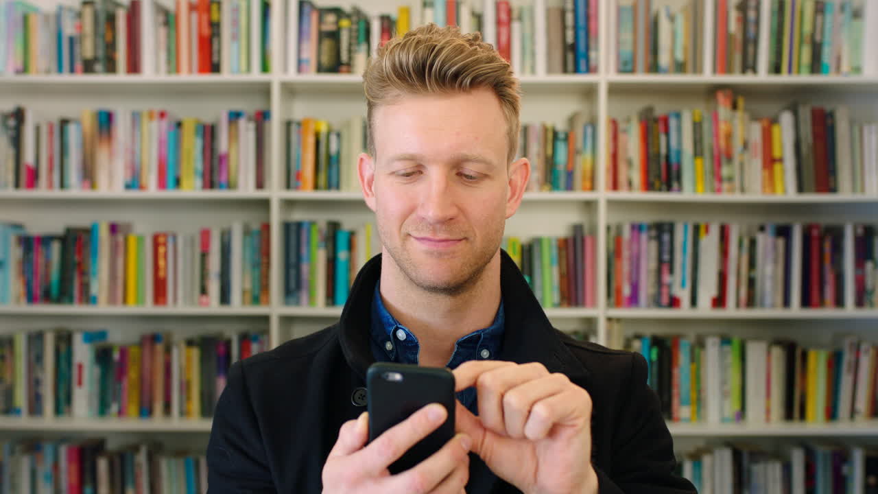 Homem moderno usando seu celular em uma livraria