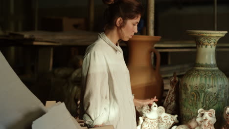 focused lady walking in studio full of pottery. woman examining products