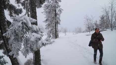 caucasian man in casual winter clothing walking in winter forest path covered with thick snow