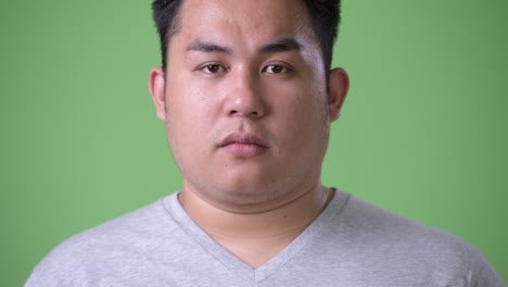 young handsome overweight asian man against green background