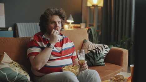 man eating chips and drinking beer while watching tv