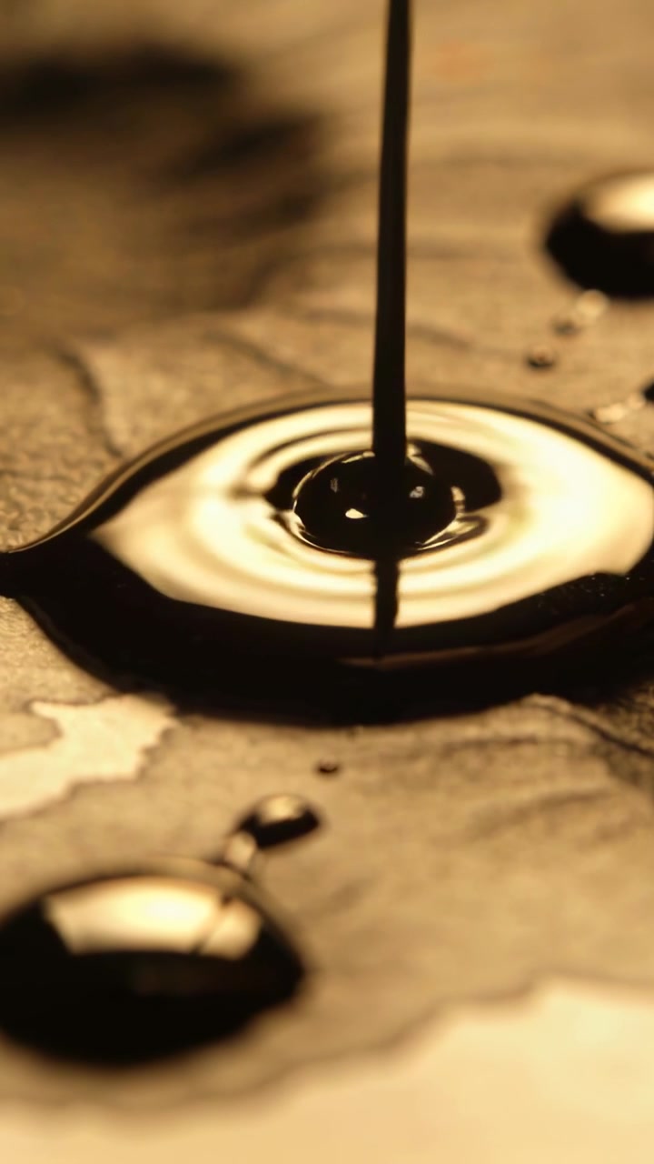 Vertical video: Falling thin stream of thick oil hitting stone, forming glossy puddle and ripples