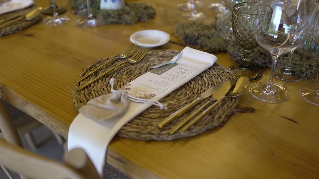 Elegant rustic wedding table setting with gold cutlery, woven placemat, and menu