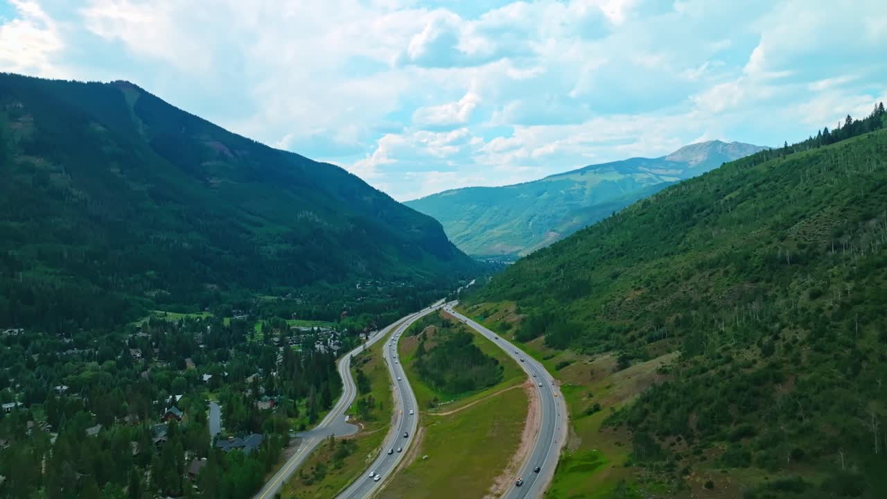 Drone of winding Vail mountain road through lush summer greenery and high alpine terrain, cars cross and zoom by