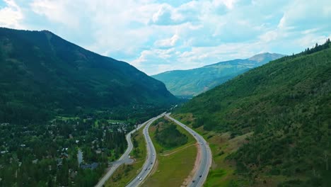 Drone of winding Vail mountain road through lush summer greenery and high alpine terrain, cars cross and zoom by
