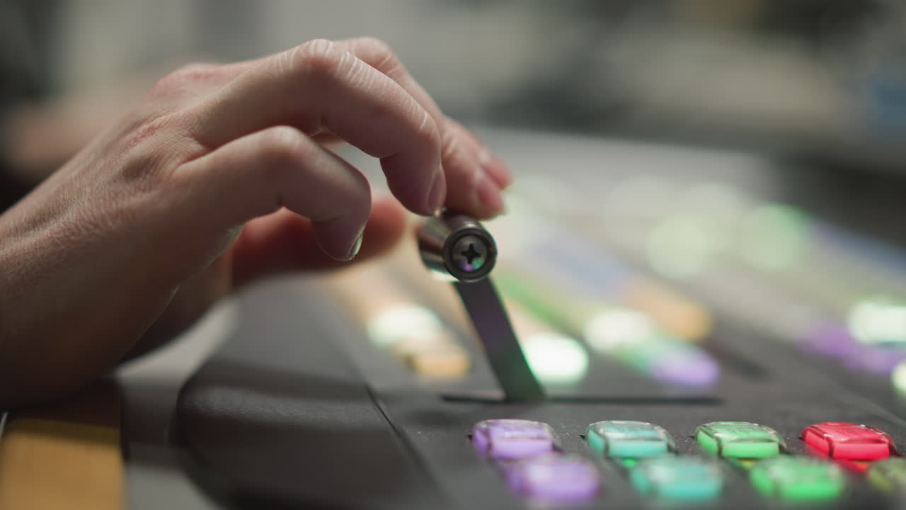 Close-up of hand pressing colored buttons on a broadcast control panel, focusing on a studio control system in a television station, operator adjusting equipment for live broadcast