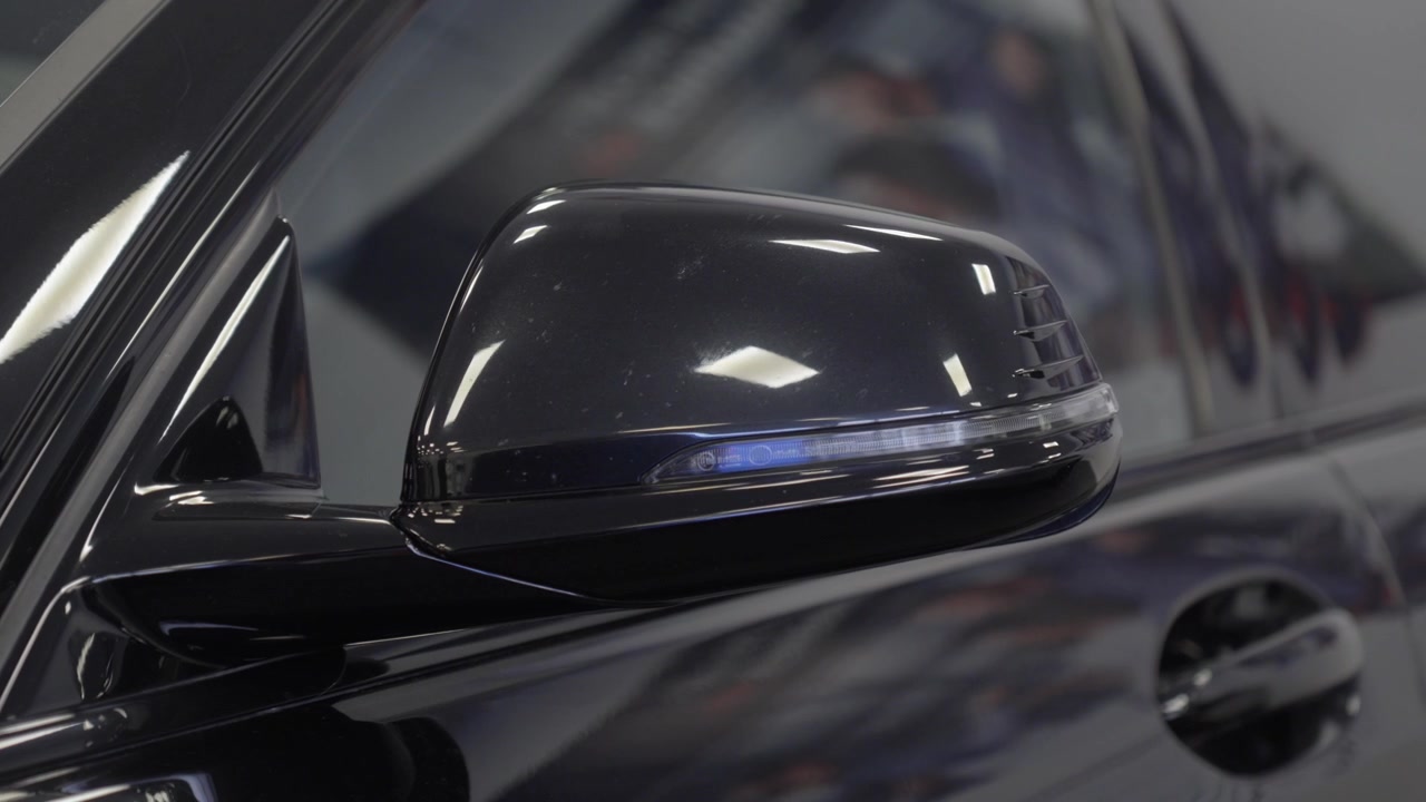 Primo piano di uno specchietto laterale di un'auto di lusso nero lucido che si apre all'interno.