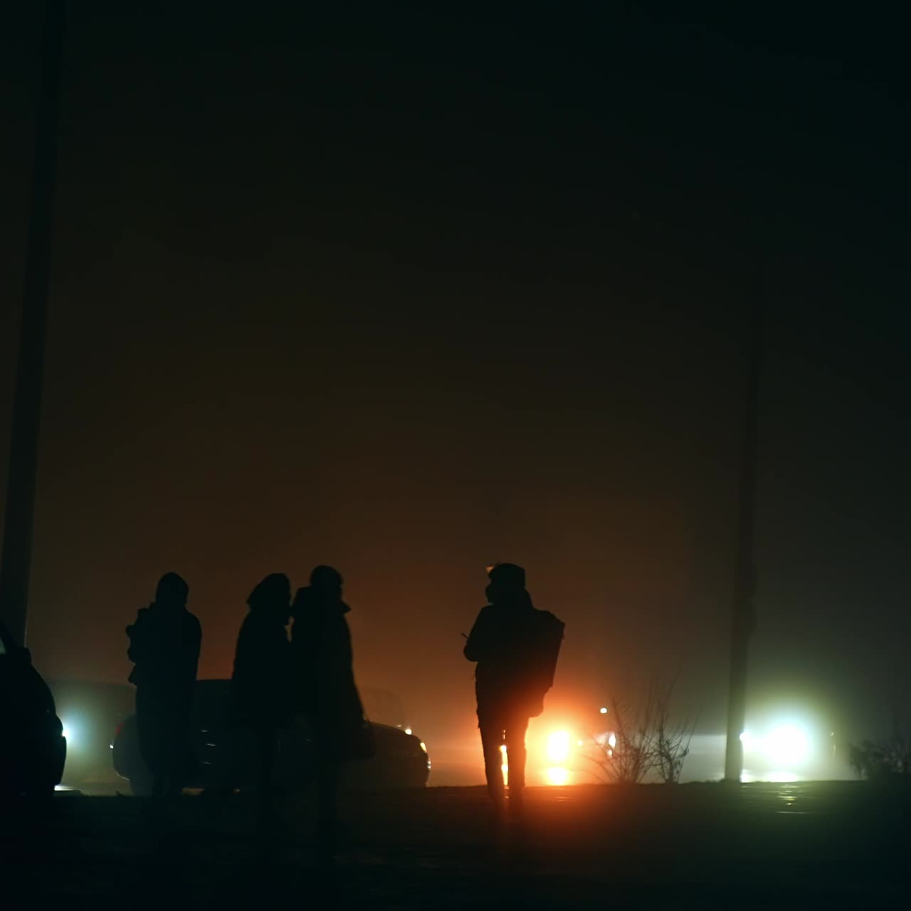 Silhouettes of people walking by the sidewalk near the road. Cars with switched on headlights ride carefully on the period of blackout