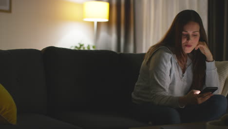 woman sitting on sofa at home at streaming or watching movie or show or scrolling internet on mobile phone 15