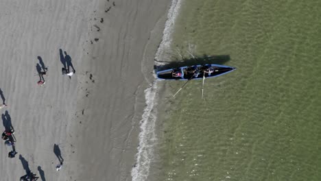 drone top down perspective follows people in currach rowing boats into open ocean water