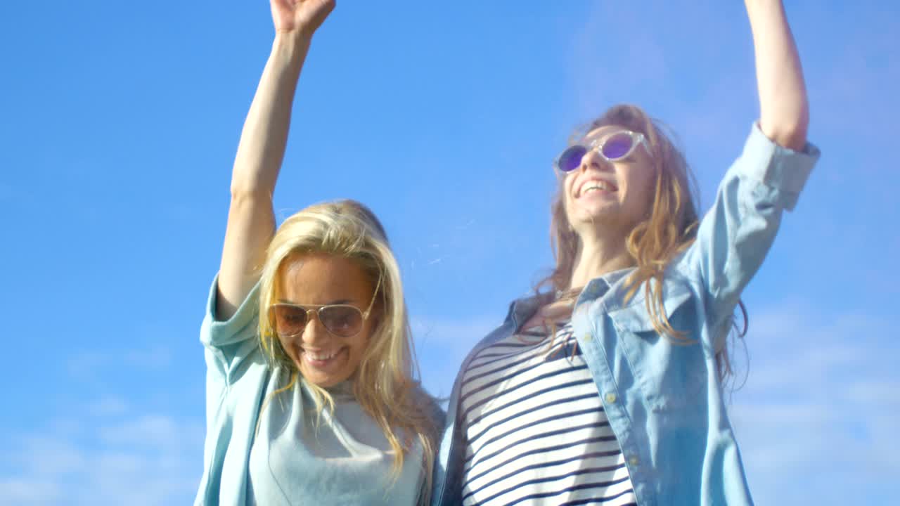 dos hermosas chicas felices se ríen y celebran el festival de holi polvo colorido volando detrás de sus espaldas. tienen el tiempo de sus vidas. cielo despejado y mar azul en el fondo.