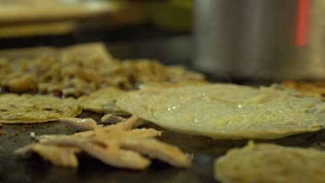 el vendedor abre una tortilla de quesadilla y la llena con carne asada y frijoles antes de servir