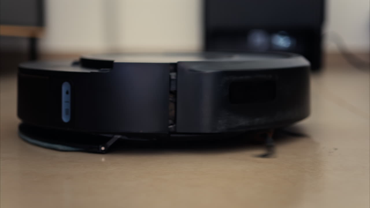 Close up of a black robot vacuum cleaner moving and rotating on the floor tiles