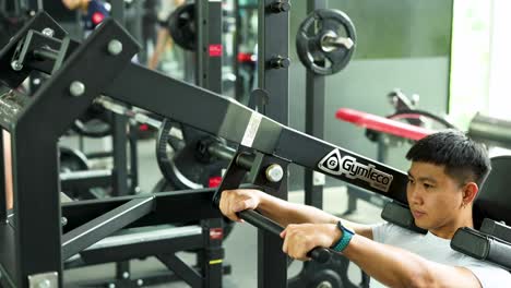 a man performs a workout on a squat machine in a well-lit gym in bangkok, thailand. the camera captures his focused effort