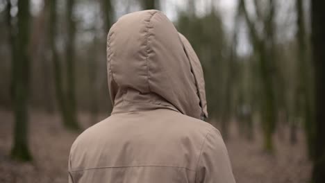 a young girl walks through the forest looking from side to side. back shot.