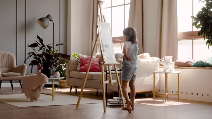 Rear View Of A Blonde Girl Painting A Plant With A Brush On A Lectern In The Living Room At Home 1