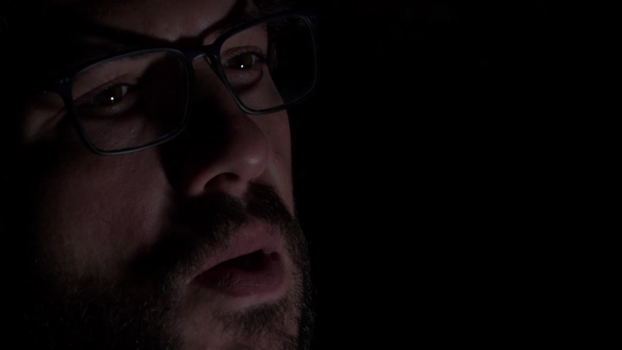 hombre barbudo con anteojos fumando cigarrillo en la oscuridad - primer plano extremo