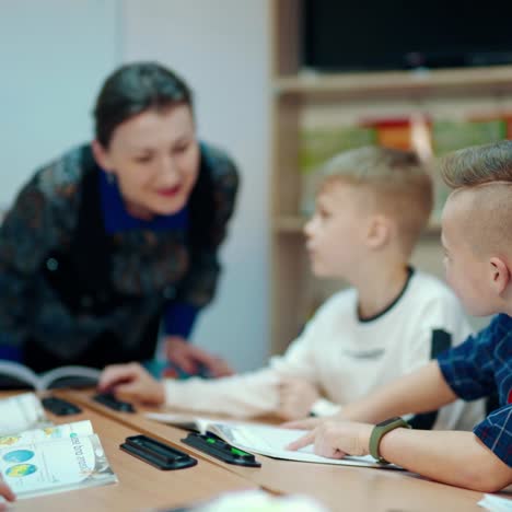 learning process at primary school. children sitting at a table in the classroom. female teacher speaking with young students. education at school.