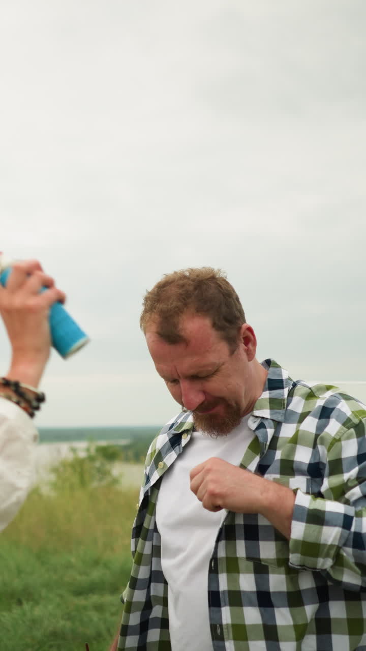 스타일리시한 모자와  드레스를 입은 여자가 울창한 잔디에서 한 남자의 머리에 모기 방제제를 스프레이합니다. 색 셔츠를 입은 남자는 여자가 그를 돌보는 동안 조용히 서 있습니다.