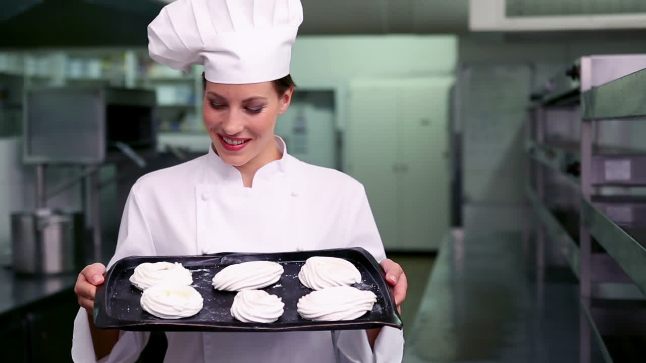 Chef felice che sorride alla telecamera mostrando un vassoio di meringhe