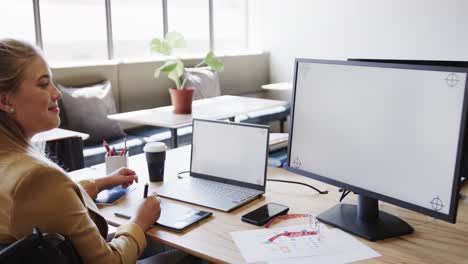 mujer de negocios caucásica en silla de ruedas usando computadora portátil y computadora con espacio de copia, en cámara lenta