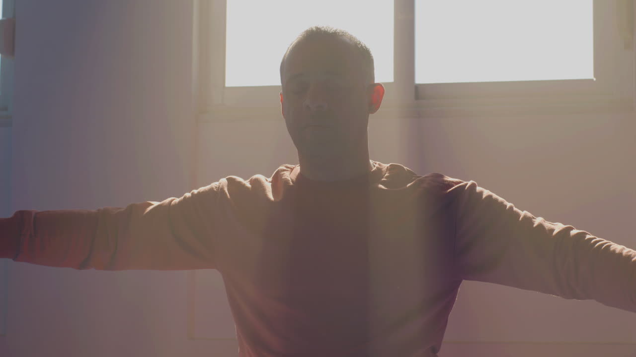 человек с закрытыми глазами сидит на полу в тренажерном зале и движет руками.