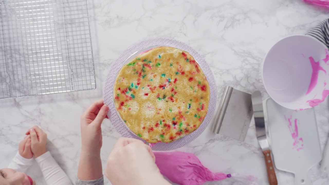 분홍색 버터크림 글래싱으로 둥근 페티 케이크 층을 글래싱합니다.