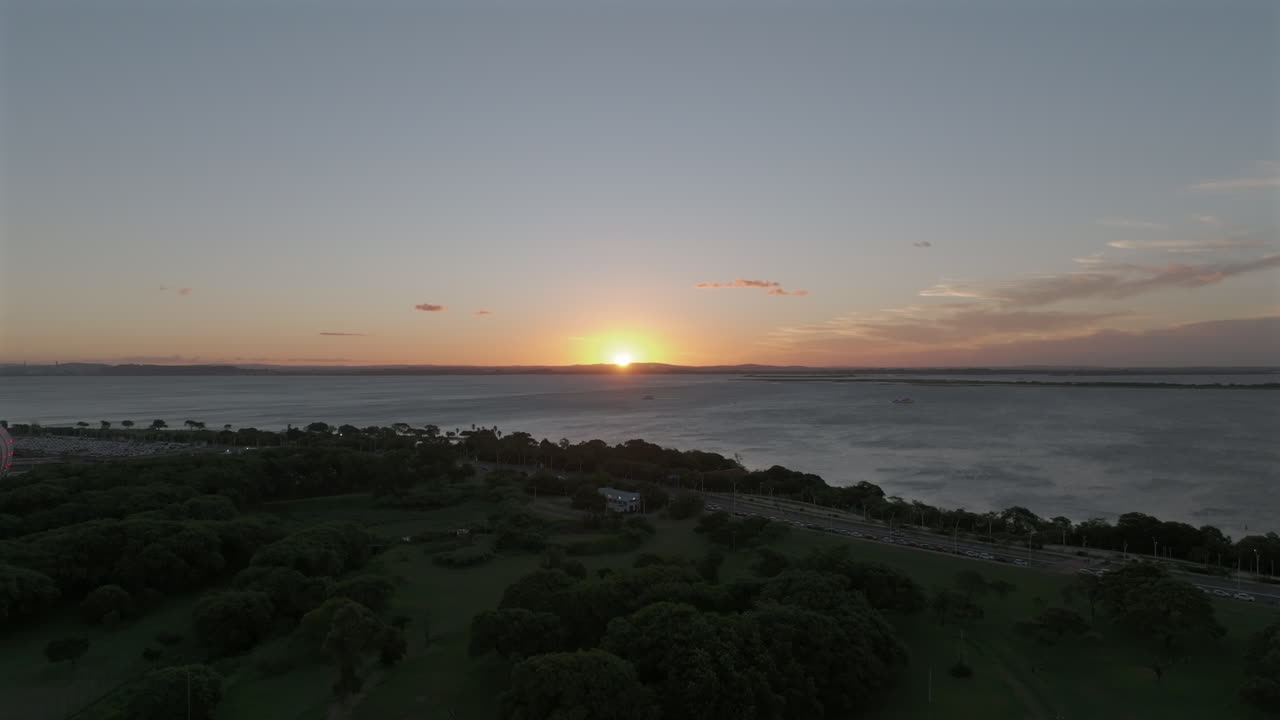 Vista aérea do pôr do sol sobre o Lago Guaíba, acima do Parque Marinha, com barcos e tráfego na orla, Porto Alegre, Brasil