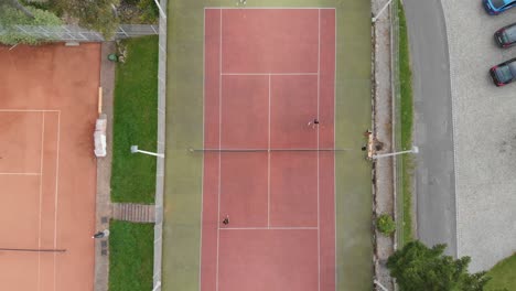 Toma-Aérea-De-Tenis-2-Contra-2-En-Cancha-De-Arcilla,-Instalaciones-Deportivas-Recreativas-Al-Aire-Libre