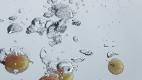 Frische-Stachelbeeren,-Fallendes-Wasser-Bildet-Blasen-Auf-Weißem-Hintergrund,-Nahaufnahme.