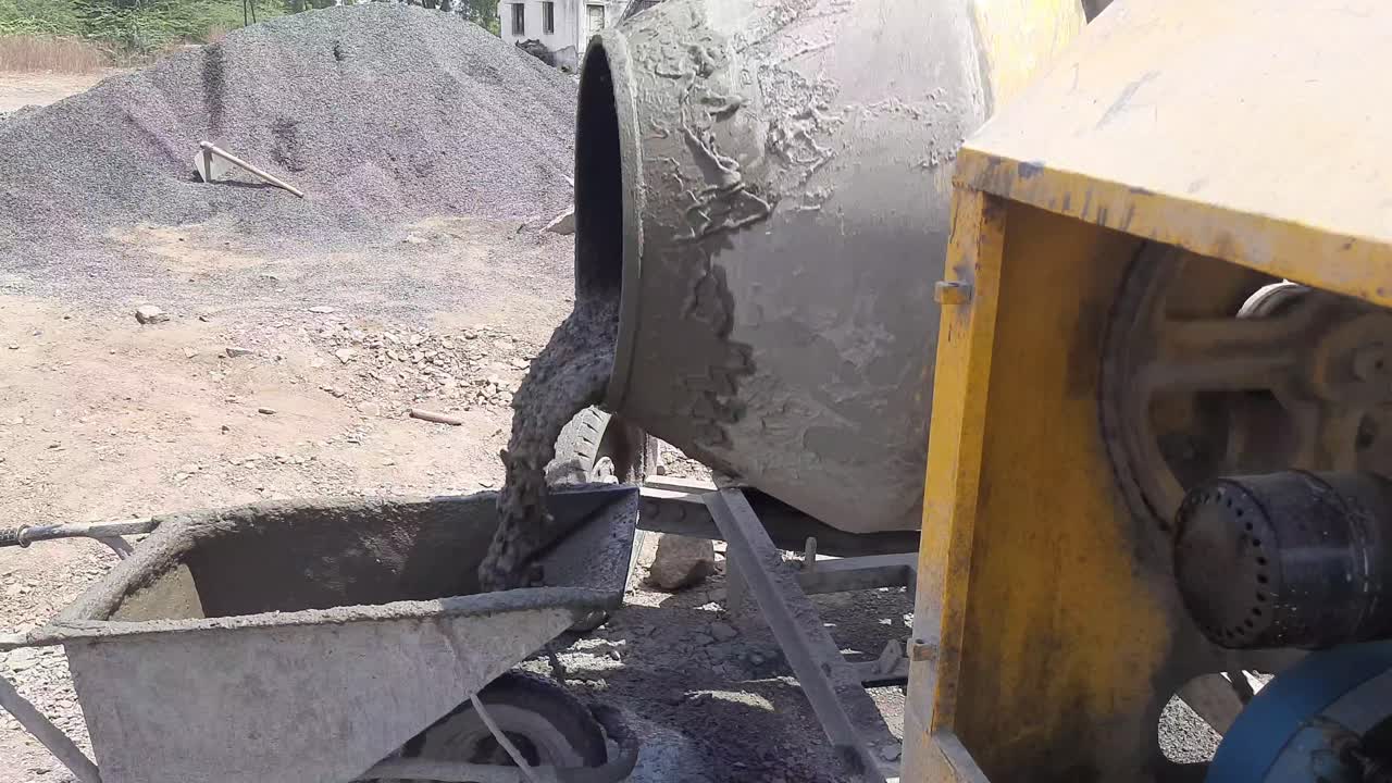 A close-up video shot of an electric concrete mixer pouring wet cement into the wheelbarrow